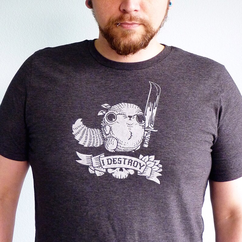 May include: A dark gray t-shirt with a graphic print of a cartoon creature holding a knife. The text "I DESTROY" is printed on a banner below the creature.