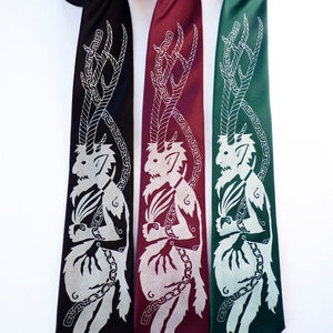 May include: Three neckties in black, burgundy, and green, each featuring a silver illustration of a horned creature with a chain design. The ties are displayed against a white background, showcasing the detailed artwork.