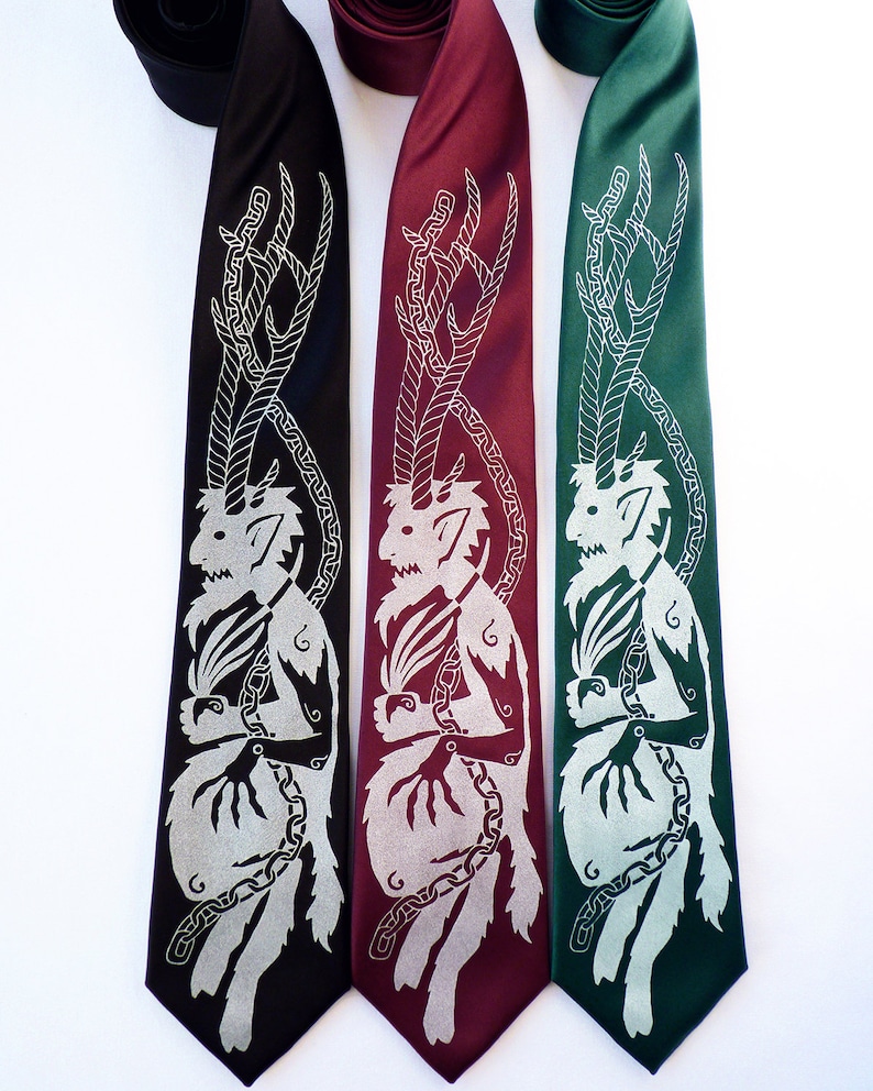 May include: Three neckties in black, burgundy, and green, each featuring a silver illustration of a horned creature with a chain design. The ties are displayed against a white background, showcasing the detailed artwork.