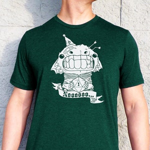 May include: A dark green t-shirt with a white graphic of a monster holding a dice with the number one on it. The monster is wearing a party hat and has a bandage on its head. The text "Nooooooooo..." is written on a banner below the monster.