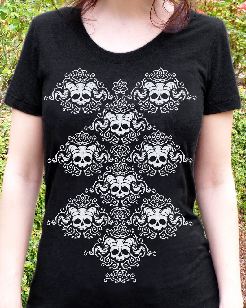 May include: Black t-shirt with a white design of stylized skulls with horns and floral accents.