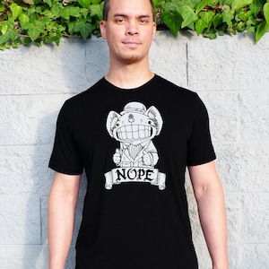 May include: A black t-shirt featuring a white graphic of a cartoon animal wearing a hat and a bow tie. The animal is giving a thumbs up and the text "NOPE" is written on a banner below it.