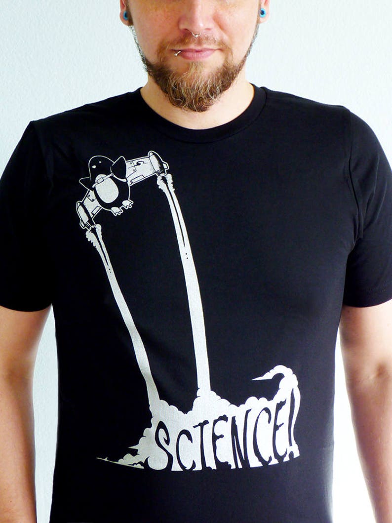 K&ouml;nnte beinhalten: Schwarzes T-Shirt mit einem wei&szlig;en Aufdruck eines Pinguins in einer Rakete, darunter das Wort "SCIENCE!". Das Design ist eine lustige, wissenschaftlich angehauchte Illustration. Der Pinguin wird in einer Rakete mit Abgasfahnen dargestellt.