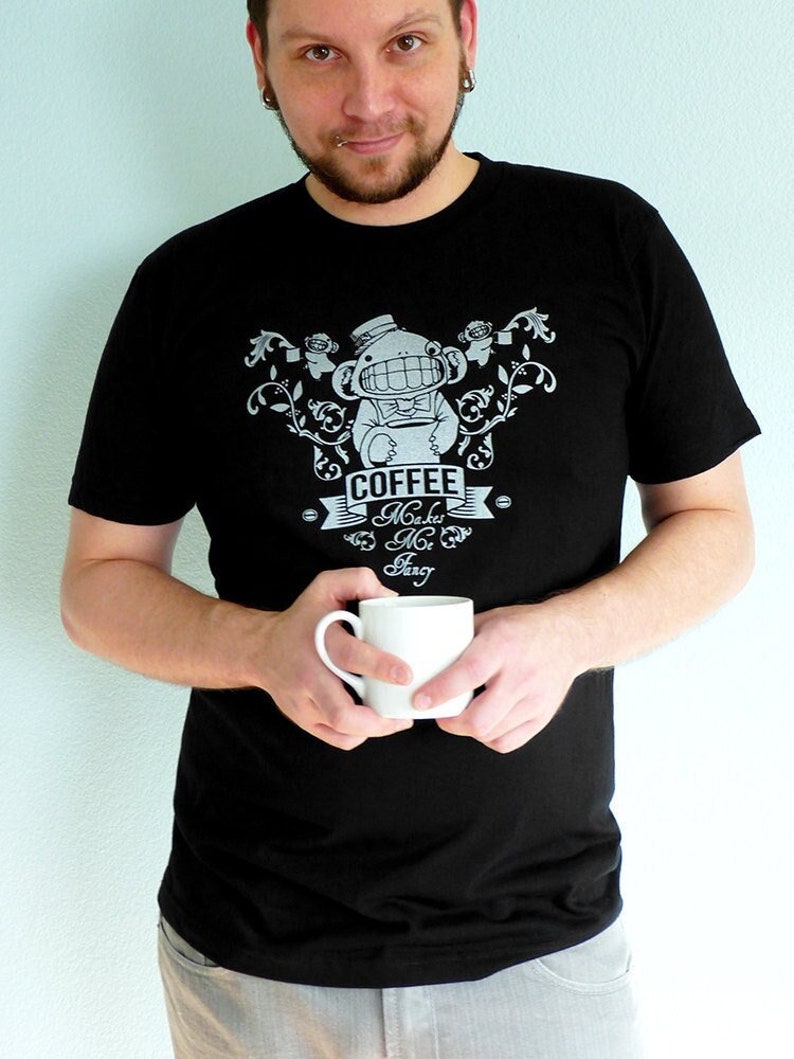 Pu&ograve; includere: Una maglietta nera con un design grafico bianco di una scimmia dei cartoni animati che tiene una tazza di caff&egrave;. Il testo sulla maglietta recita "Coffee Makes Me Zing".