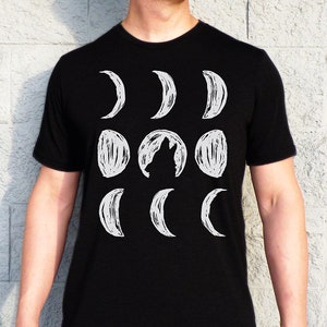 May include: A black t-shirt with a white graphic of a wolf howling at the moon. The moon is depicted in various phases, from a crescent to a full moon.