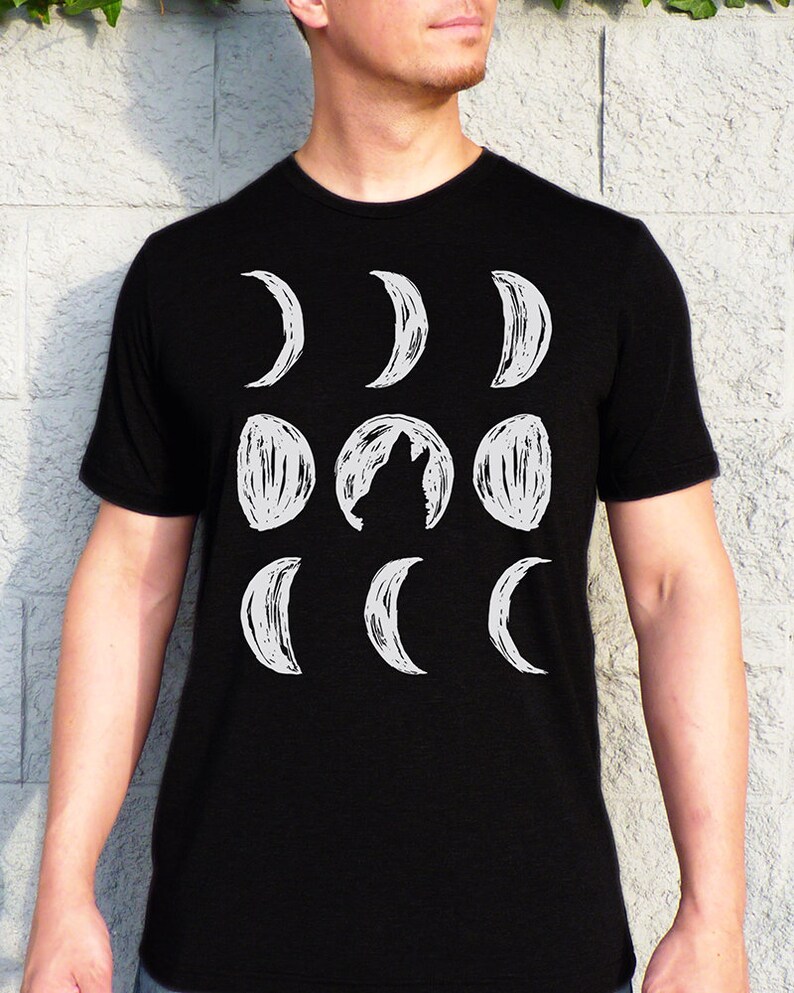 May include: A black t-shirt with a white graphic of a wolf howling at the moon. The moon is depicted in various phases, from a crescent to a full moon.