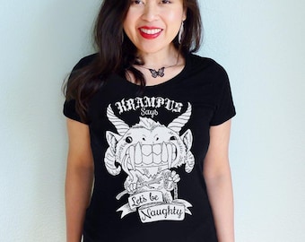 May include: Black t-shirt featuring a white illustration of a horned creature with the text "Krampus Says" above and "Let's be Naughty" below. The graphic tee is a crew neck style.