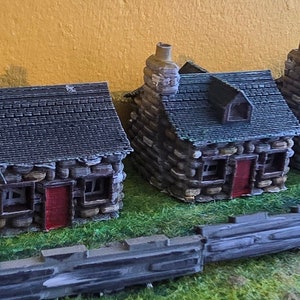 May include: A row of six miniature stone houses with red doors and gray slate roofs. The houses are arranged on a green grassy surface with a gray stone wall in front.