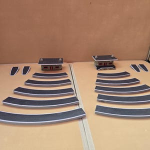 May include: A diorama set with miniature buildings, curved road segments, and small rectangular pieces. The buildings have dark grey roofs and red accents. The road pieces are black with white edges.
