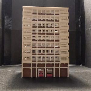 Peut inclure: Modèle blanc d'un immeuble haut avec de nombreuses fenêtres et deux portes rouges en bas.
