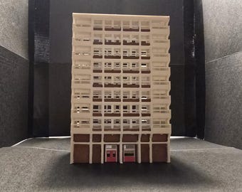 May include: A white model of a tall building with many windows and two red doors at the bottom.