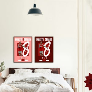 May include: Two digital prints of a soccer player in a red and white uniform with the text "Maestro Deard" and the number "8" in white. The print on the left has the text "Arsenal" below the number and the print on the right has the text "Real" below the number. The prints are displayed on a white wall above a bed with white bedding.