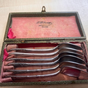Pode incluir: Um conjunto de seis colheres de chá de prata numa caixa de madeira forrada a veludo verde e rosa. A caixa tem um rótulo que diz "J. Robinson Sheffield".
