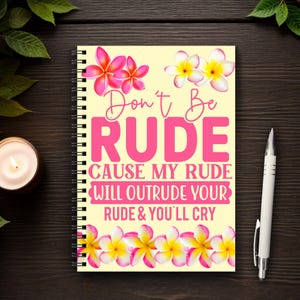 May include: A yellow spiral notebook with a pink and white floral design. The notebook has the text "Don't Be Rude Cause My Rude Will Outrude Your Rude & You'll Cry" printed on the front.