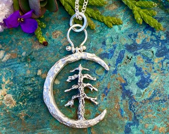 Puede incluir: Un collar de plata con un colgante de media luna con un diseño de árbol texturizado. El colgante está unido a una cadena de plata con un cierre simple.