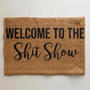May include: A brown doormat with the text "Welcome to the Shit Show" in black lettering.