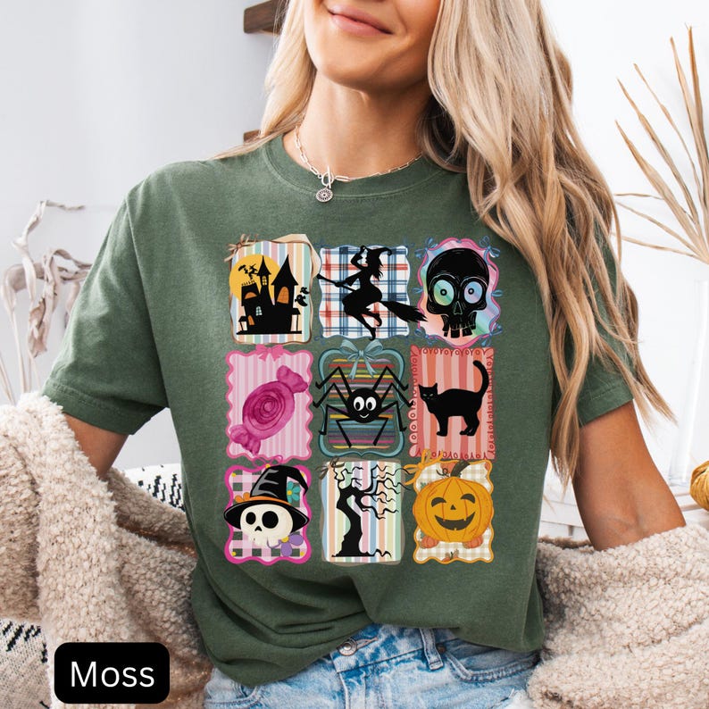 Puede incluir: Camiseta verde musgo con una cuadr&iacute;cula de gr&aacute;ficos tem&aacute;ticos de Halloween. Los gr&aacute;ficos incluyen una casa embrujada, una bruja en una escoba, una calavera, caramelos, una ara&ntilde;a, un gato negro, una calavera con un sombrero de bruja, un &aacute;rbol espeluznante y una calabaza. La palabra "Moss" est&aacute; impresa en la parte inferior.