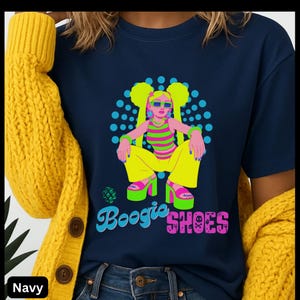 May include: Navy blue t-shirt featuring a colorful graphic of a cartoon character wearing sunglasses and platform shoes. The character is surrounded by blue dots and the words "Boogie Shoes" in a retro font.