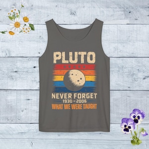 May include: A gray tank top with a retro design featuring the word "PLUTO" in distressed orange letters. Below, a graphic of Pluto is set against a striped background of orange, red, and yellow. The text "NEVER FORGET 1930-2006 WHAT WE WERE TAUGHT" is below.