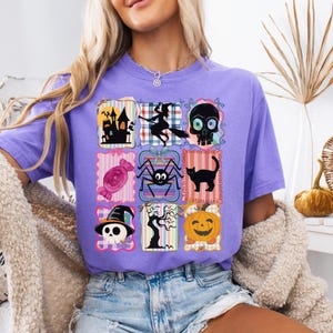 Puede incluir: Una camiseta de color lila claro con una cuadr&iacute;cula de parches con tem&aacute;tica de Halloween. Los parches incluyen una casa embrujada, una bruja en una escoba, una calavera, un caramelo, una ara&ntilde;a, un gato negro, una calavera con sombrero de bruja, un &aacute;rbol desnudo y una calabaza.