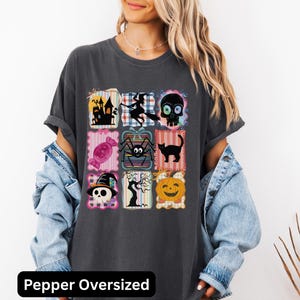 Puede incluir: Camiseta gris oscuro de gran tama&ntilde;o con una cuadr&iacute;cula de ilustraciones tem&aacute;ticas de Halloween. El dise&ntilde;o incluye una casa embrujada, una bruja, una calavera, caramelos, una ara&ntilde;a, un gato negro y una calabaza. El texto "Pepper Oversized" est&aacute; en la parte inferior.
