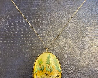 May include: A gold chain necklace with an oval pendant featuring a hand-painted scene of people riding horses in a landscape. The pendant is surrounded by a decorative gold border.