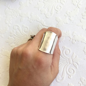 May include: A wide silver band ring with a smooth, polished finish. The ring is worn on a finger.