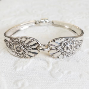 May include: A silver bracelet made from a repurposed spoon with a floral design. The bracelet is open and has a clasp.