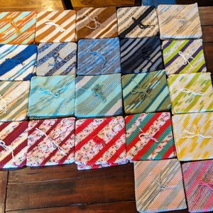 Pode incluir: Uma coleção de 24 quadrados de crochê em várias cores e padrões, incluindo listras, listras diagonais e designs texturizados. Os quadrados estão dispostos em filas sobre uma mesa de madeira.