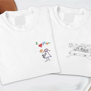 May include: Two white t-shirts with crew necks. One shirt features a colorful embroidered drawing of a person holding flowers with the text "I ❤️ Mom." The other shirt has a black embroidered school bus with children.