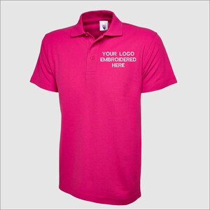 May include: A pink polo shirt with short sleeves and a white embroidered logo that says "YOUR LOGO EMBROIDERED HERE".