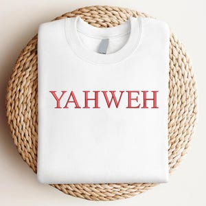 May include: A white crewneck sweatshirt featuring the word YAHWEH embroidered in red capital letters across the center of the chest. The garment has a ribbed collar and long sleeves, presented in a clean, folded layout for clear visibility.