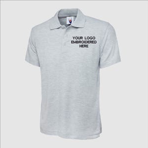 May include: A gray polo shirt with short sleeves and a button-up collar. The shirt has the text "YOUR LOGO EMBROIDERED HERE" on the front.