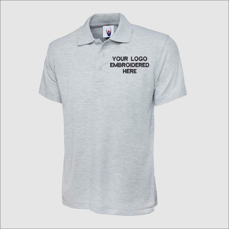 May include: A gray polo shirt with short sleeves and a button-up collar. The shirt has the text "YOUR LOGO EMBROIDERED HERE" on the front.