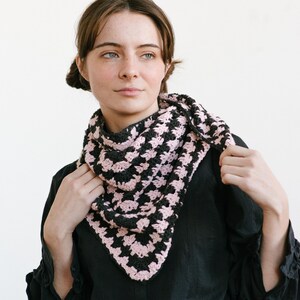 May include: A woman wearing a black button-down shirt and a pink and black crocheted scarf.