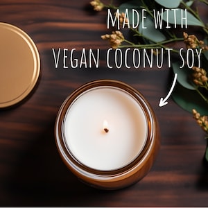 May include: A lit candle in a brown glass jar with a gold lid. The candle is made with vegan coconut soy wax. The text "MADE WITH VEGAN COCONUT SOY WAX" is written in white above the candle.