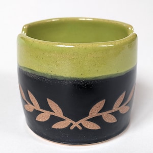 May include: A green and black ceramic dish with a gold leaf design. The dish has a wide rim and a rounded bottom.
