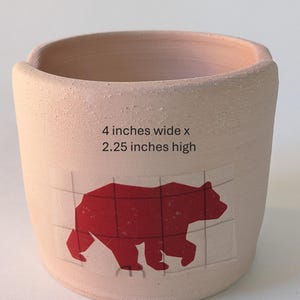 May include: A light pink ceramic planter with a red bear silhouette design. The planter is 4 inches wide and 2.25 inches high.
