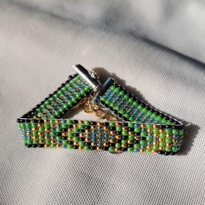 May include: A green, blue, gold, and black beaded bracelet with a silver clasp.