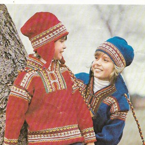 May include: Two children wearing red and blue knitted jumpers with matching hats. The jumpers have colourful geometric patterns and the hats have ear flaps. The jumpers are labelled "OSLO" and "M2063".