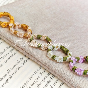 May include: A collection of handcrafted macramé rings in shades of yellow, cream, green, and lilac. The rings are linked together, demonstrating detailed knotwork. The rings are presented on a neutral-coloured fabric, showcasing the craftsmanship.