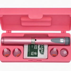 May include: A pink plastic carrying case containing a metallic pink injection pen with a gray display window showing the number zero. The case includes four small clear plastic caps and a white Curad alcohol pad packet with black text.
