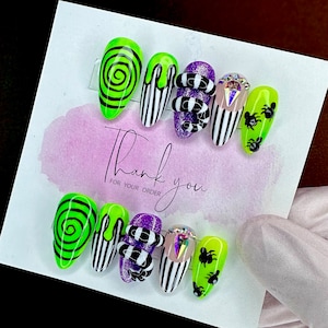 Könnte beinhalten: Set mit zehn grünen und schwarzen Halloween-Press-on-Nägeln mit verschiedenen Designs, darunter eine Spirale, Streifen und eine Schlange. Die Nägel werden auf einer weißen Karte mit dem Text "Vielen Dank für Ihre Bestellung" angezeigt.