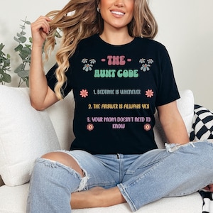 May include: A black t-shirt with the text "The Aunt Code" and a list of rules: "Bedtime is whenever", "The answer is always yes", and "Your mom doesn't need to know". The text is in a retro font with colorful flowers.