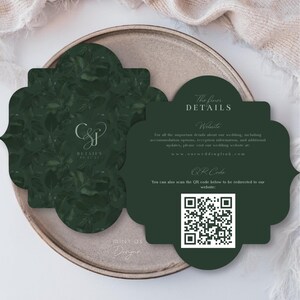 Peut inclure: Carte de d&eacute;tails de mariage vert fonc&eacute; avec un motif floral et les initiales "CSJ". La carte comprend le texte "The finer DETAILS", des informations sur le site Web et un code QR. La carte est sur une assiette de couleur neutre.