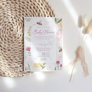 May include: Baby shower invitation with a floral and bee theme. The invitation features the text "Baby Shower" in pink script, along with details and a honeycomb design. The invitation is on a white background with floral and bee illustrations.