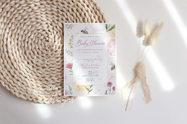 May include: Baby shower invitation with a floral and bee theme. The invitation features the text "Baby Shower" in pink script, along with details and a honeycomb design. The invitation is on a white background with floral and bee illustrations.