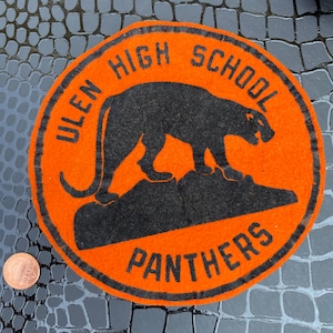 May include: A vintage orange felt patch with black lettering and a black panther silhouette. The patch reads "Ulen High School Panthers".