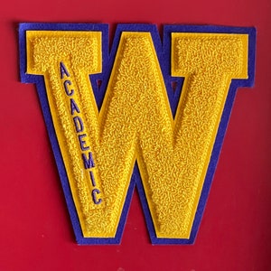 May include: A large yellow felt letter W with a purple felt border. The letter W has the word "ACADEMIC" embroidered vertically down the left side.
