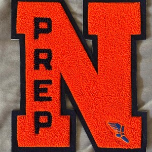 May include: Orange felt letter N with black outline and a smaller blue felt winged foot logo. The letter N has the word "PREP" vertically written on the left side.